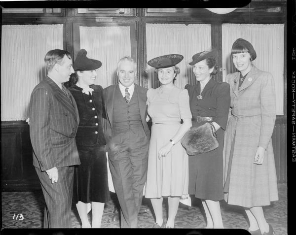 Charlie Chaplin grinning for the camera in the middle of a group of four women and a man in a meeting at the Waldorf Astoria related to the New York premiere of "The Great Dictator."