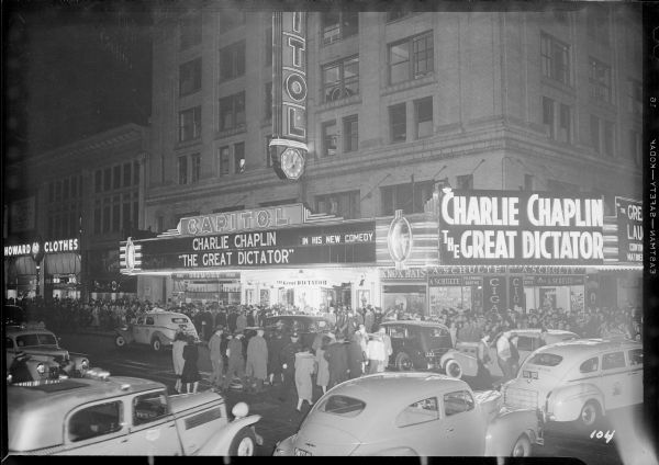 Crowds gather under the marquee of the Capitol Theatre for the New York premiere of Charlie Chaplin's "The Great Dictator" the evening of October 15, 1940. The photograph was taken catercorner from the theater at the intersection of West 51st Street and Broadway with traffic and pedestrians in the foreground.