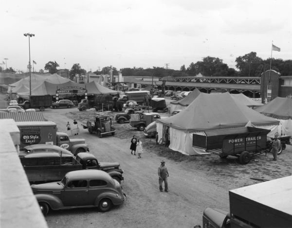 Elevated view of the back stage area of the Wisconsin Centennial Exposition at the State Fair Park. Permanent and temporary structures are visible, as are delivery vehicles and farm equipment.