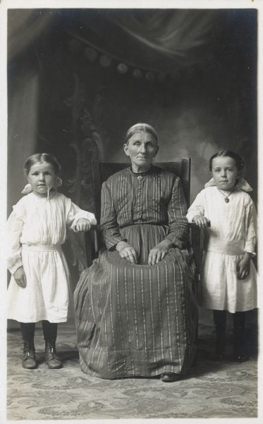 The woman, Mary Zehnpfennig Bachmayer, is seated in this studio portrait. Her daughters Lucy and Kunigunda Helene stand next to her.