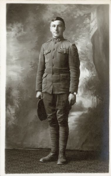 Full-length studio portrait of Englebert Boehnen. He is standing proudly in his World War I military uniform in front of a painted backdrop.