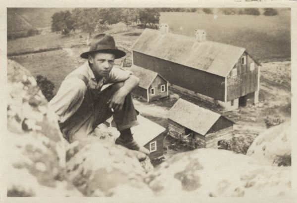 A man poses on a bluff overlooking a farm in the valley below.