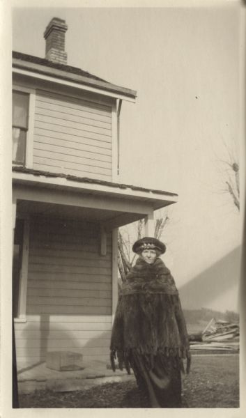 Miss Emma Strauss poses near a house wearing a fur coat and fancy hat.