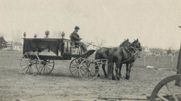 Black Earth hearse drawn by horses. Chris Schanel, the Black Earth undertaker, is driving. In the background on the right a small pig is running near a fence.