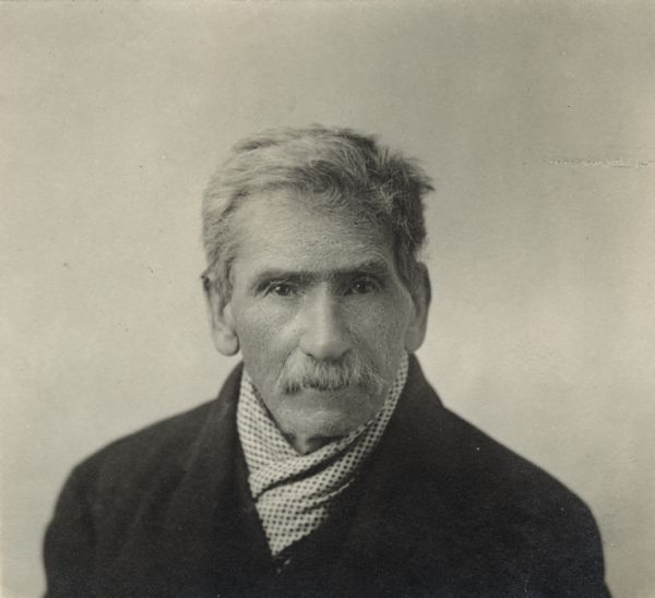 Quarter-length portrait of unidentified man with a moustache. He is wearing a jacket and polka dot scarf.