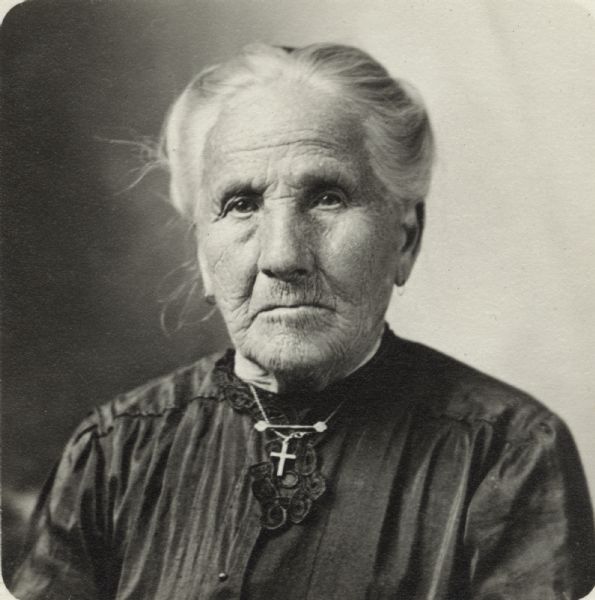 Quarter-length portrait of unidentified woman. She is wearing a dark dress and a crucifix on a chain.