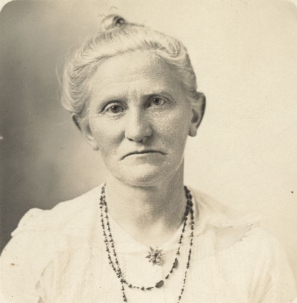 Quarter-length portrait of unidentified woman wearing a light-colored dress, pin and necklace. Her hair is up in a bun.