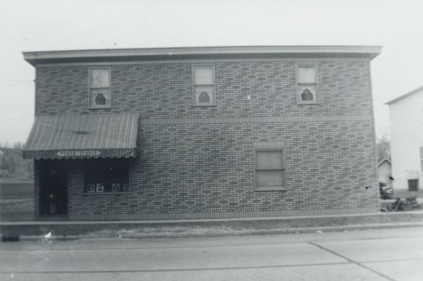 Exterior view of Matthew Witt's Photography Studio. A woman is barely visible standing in the doorway, under the awning. Framed photographs are on display in the window.