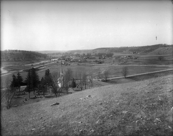 View down valley towards the back of the Lutheran Church and cemetery. Houses and barns are in the valley below, and more hills are in the far background. Seen from Lutheran Church Hill.