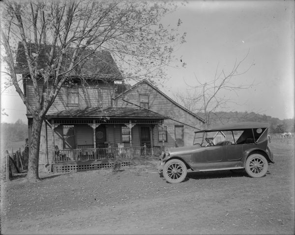 View of the exterior of the first home of Matthew Witt, photographer. An automobile is parked in the yard.
