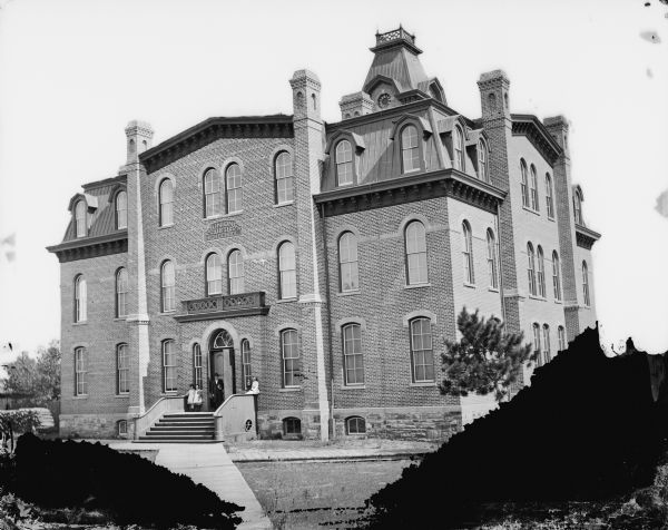 Union High School, constructed in 1871. It later probably became a grade school. A man, woman and three children are posed sitting and standing on the steps. Negative painted in the upper half.
