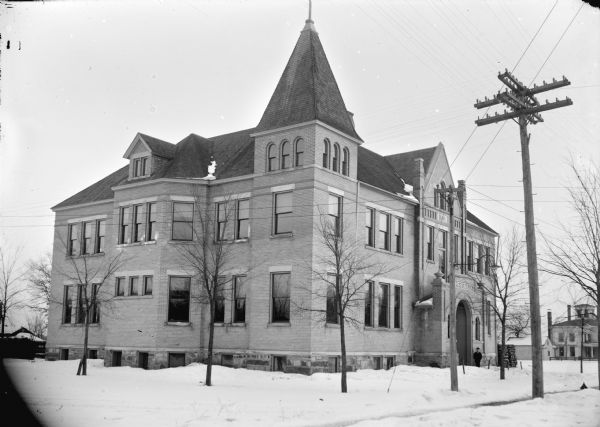 High school constructed in 1897, surrounded by snow-covered ground and a man posed standing by the entrance.