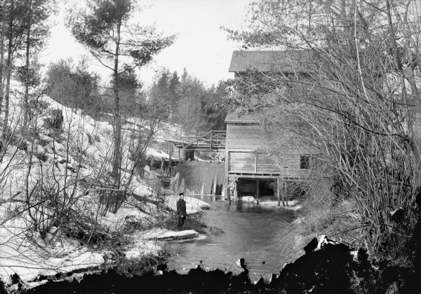 Man posed standing on a bank in front of the grist mill located on Squaw Creek, probably operated by Narracong and later Loesching, and then possibly Johnson. There was a carding mill about half a mile downstream on the John Hanson farm until about 1905, then another half mile downstream was the Charter Oak Mill. The Narracong Mill was the most famous, and later became a night club.	