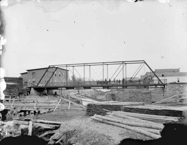 View from what appears to be a lumber yard of men posed standing on the newly constructed Harrison Street bridge that replaced one destroyed in the flood of 1911. There is a horse-drawn vehicle going across the bridge, and there also appear to be some cattle on the bridge near a group of men.
