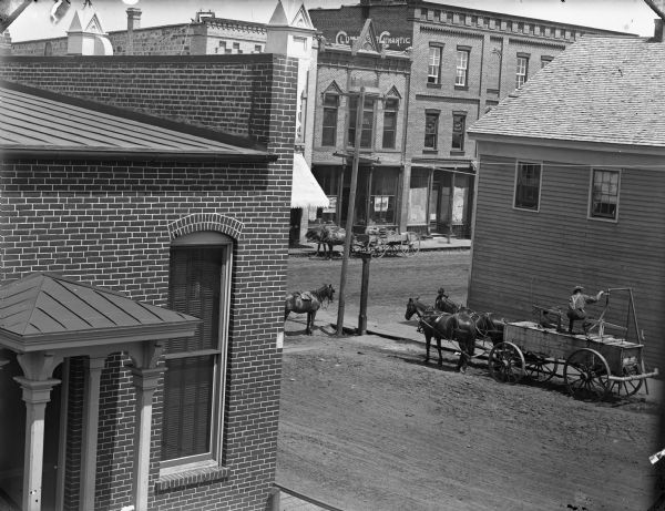 Elevated view of man filling a street sprinkler or "water wagon" pulled by two horses near the intersection of First and Main Streets.