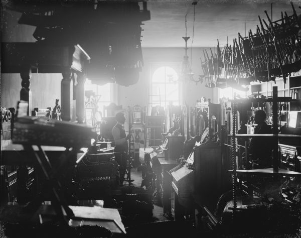 Interior of a furniture store, with two men posed among the rows of furniture. A group of chairs hangs from the ceiling.