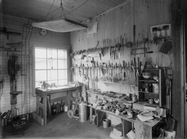 Interior of a workshop, probably owned by Leslie Werner, showing tools on the walls, a drill press, and a workbench in front of a window.
