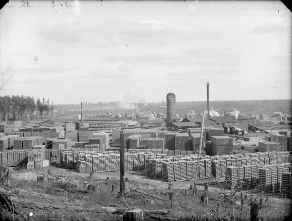 View from hill of lumber operation, with stacks of timber and a sawmill in operation, probably McKenna in eastern Jackson County.