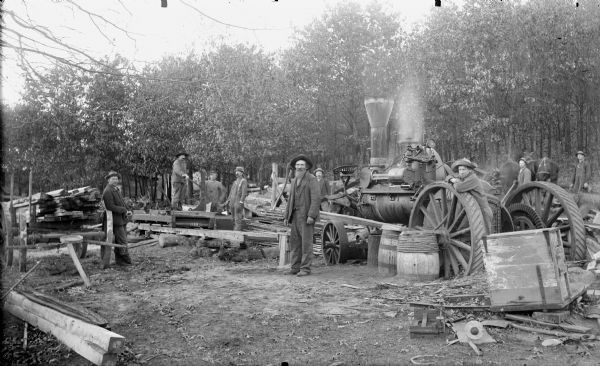 Men posed using a steam-powered open-air saw, probably using a steam tractor for power.