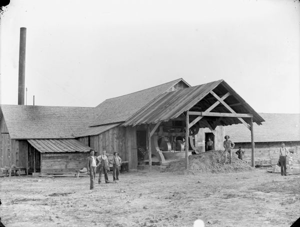 Halcyon Brick Yard, men and a young boy are posed standing in front of and inside a wooden building with machinery.
