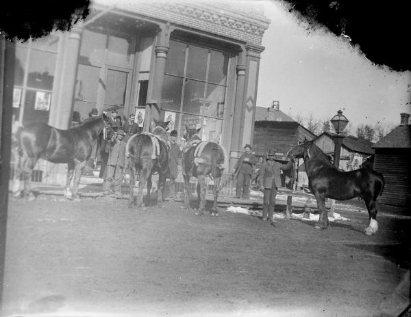 Three men displaying four horses in front of a storefront, probably the Jones Lumber and Merchandise on Water Street.	