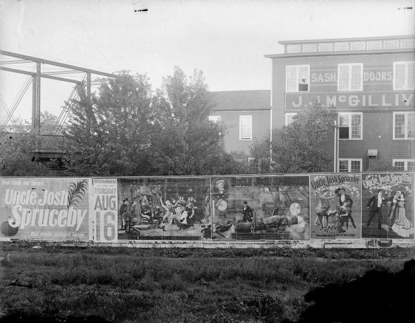 Billboard in front of the J.J. McGillivray Sash and Door Factory advertising "That funny old farmer Uncle Josh Spruceby Has made millions laugh. Opera House, one night only, Thursday, Aug. 16."	