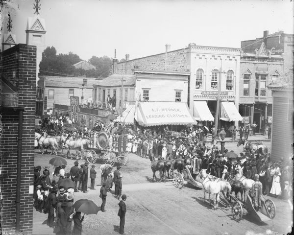 Elevated view of crowd gathered at the intersection of First and Main Streets to watch a calliope and chariot riders in a circus parade, probably the Ringling Brothers Circus.