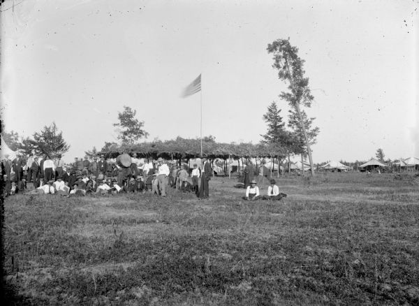 Group of men and drum posed in front of an arbor and an American flag. Native American powwow held six miles east of town.