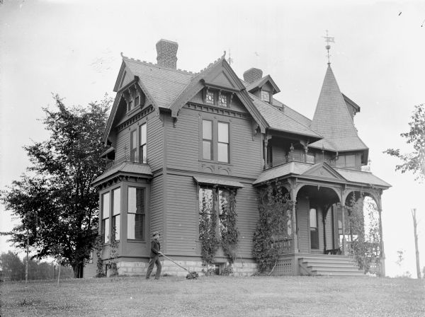 Boy mowing the lawn in front of an elaborate Victorian frame house, probably the residence of W.R. O'Hearn located at Tenth and Harrison Streets. The house was later set on fire by A.J. McNab.