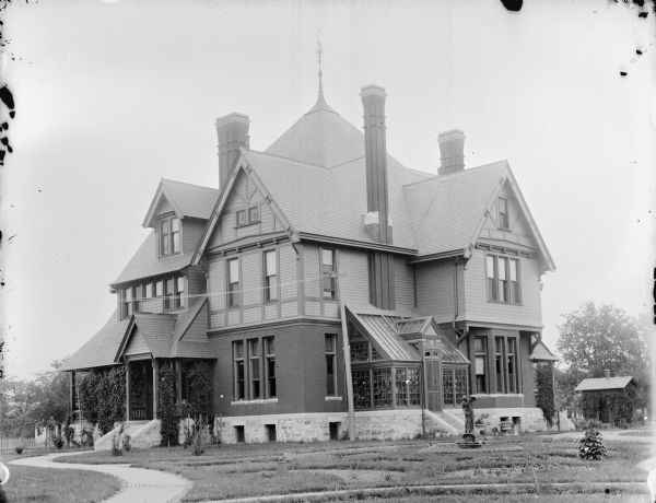 Large three-story home with an attached greenhouse. There is a small statue and fountain in the yard, and a curved brick walkway. Probably the home of W.T. Price.