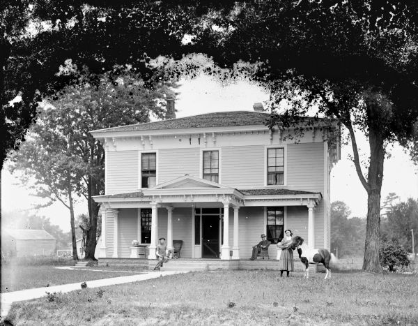 View across lawn of the Roddy House. A young girl is posing in the yard standing and displaying a pony, a young man is sitting with a dog near the porch steps, and another man is sitting in a chair on the porch of the frame house. Pottery vessel are displayed on pedestals on the left and right side of the porch. Probably the residence of T.R. Roddy.	