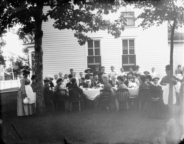 Large group posed sitting and standing around a long table in front of a two-story frame house, probably the W.T. Murray home at Tenth and Main Streets.