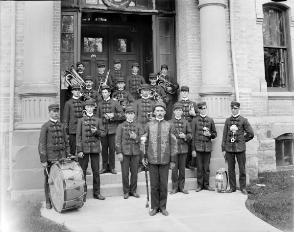 Band posed standing on the steps of a brick building, probably the Alma Center Band in front of the Jackson County Courthouse.