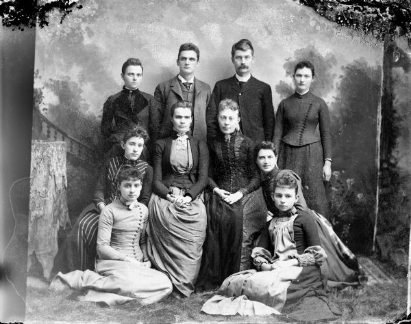 Studio portrait in front of a painted backdrop of eight women, six sitting and two standing, and two standing men.