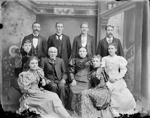 Studio portrait of a seated elderly man and woman, surrounded by four seated women and four standing men. Probably the Ulrich Olderboltz family. Standing, from left to right, Frank (drowned during the flood of 1911, took a week to find the body), Ed/Paddy, Charley (drowned in a vat of beer), and George. Sitting, from left to right, Emma Olderboltz Stokley, Mary, Ulrich Olderboltz, Mother Olderboltz, Anna, and Emma.	