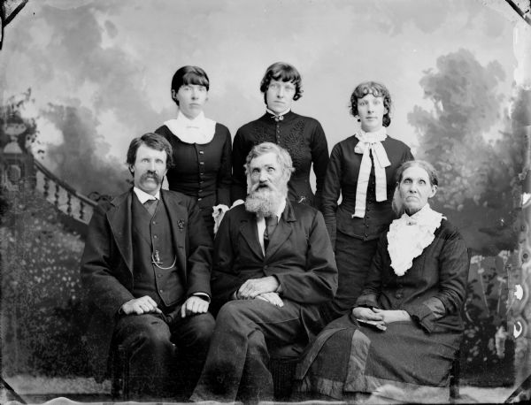 Studio portrait in front of a painted backdrop of elderly couple with their grown children.