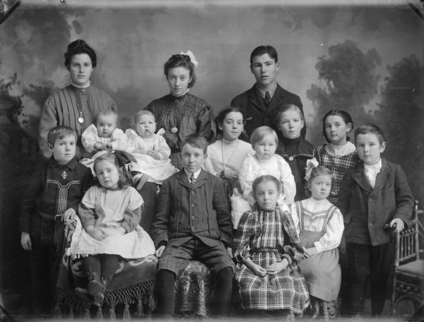 Studio portrait in front of a painted backdrop of two women and a young man posed standing behind twelve children.