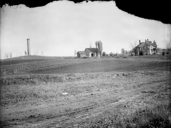 View across field of a large house and barn. The city water tower is on a hill on the left. Probably the farm of Will O'Hearn.