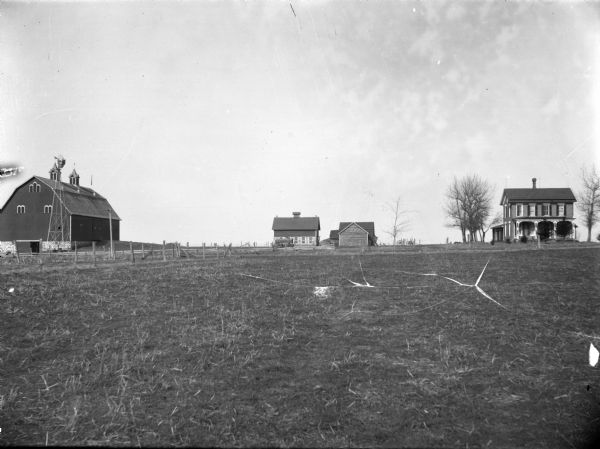View across field of frame house, barn, and farm buildings.