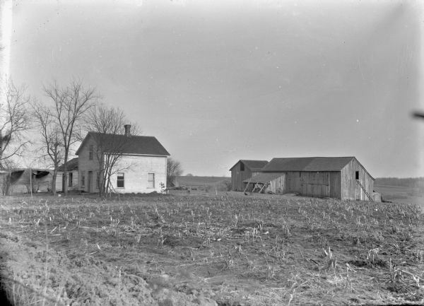View across harvested field, of what was probably corn, of frame house and barn.
