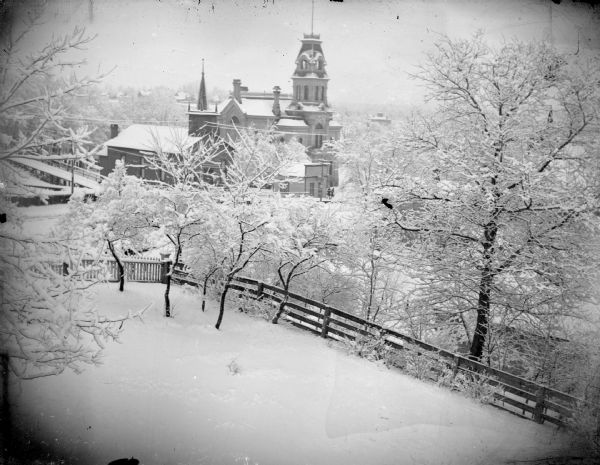 Elevated view of the Jackson Country Courthouse and church from a hill. In the foreground is a snowy yard, fence, and trees.