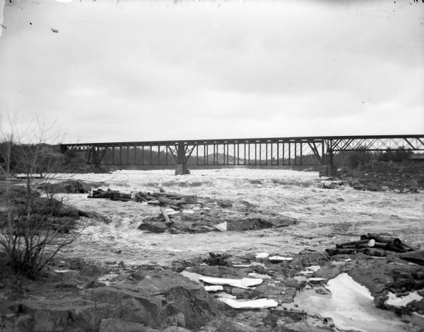 Winter view of the railroad bridge over the river. There are signs and graffiti painted on the rocks below in the foreground.