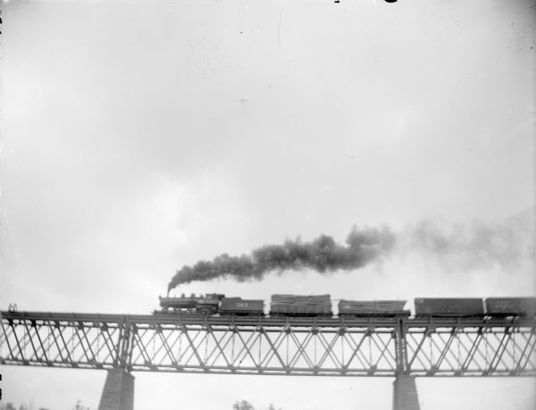 View looking up towards a locomotive and five railroad cars on a railroad bridge crossing a river.	