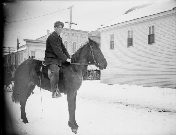 Man posing mounted on a horse on a snow-covered street. Commercial buildings are in the background.