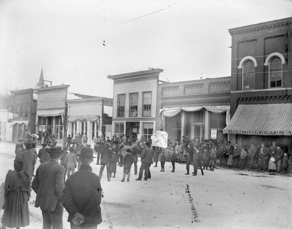 Crowd gathered on Main Street to see a poster and hear a band announcing the "Buchanan Comedy, Tonight."	