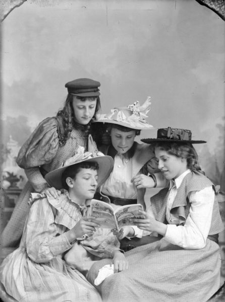 Studio group portrait in front of a painted backdrop of four young women posing looking at a copy of "Outdoors Magazine."
