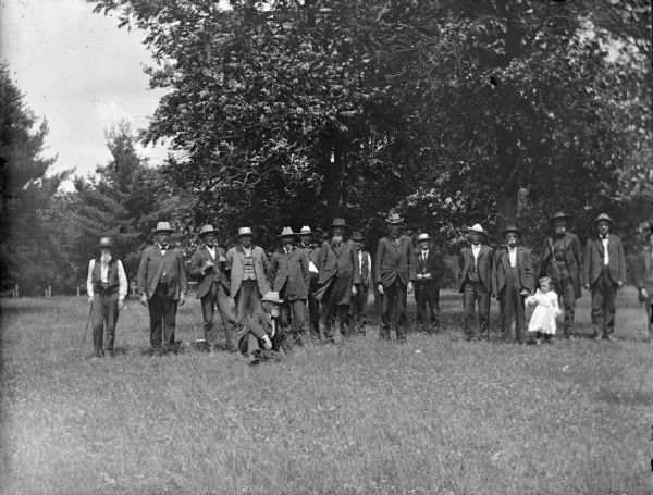 View across field towards a group of men and a young girl posing in a field. In the background are trees.