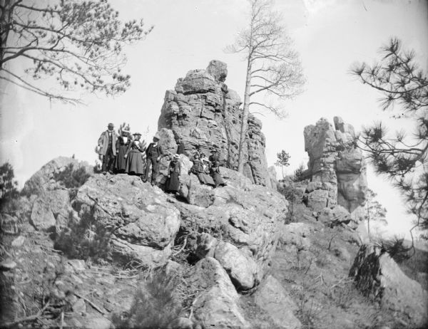 View looking up towards a group of eight women and three men posing sitting and standing on a rock outcroppings.