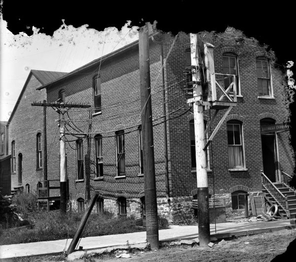 View from unpaved street of telephone wires and poles in front of the American Express Building and the photography studio of Charles J. Van Schaick.