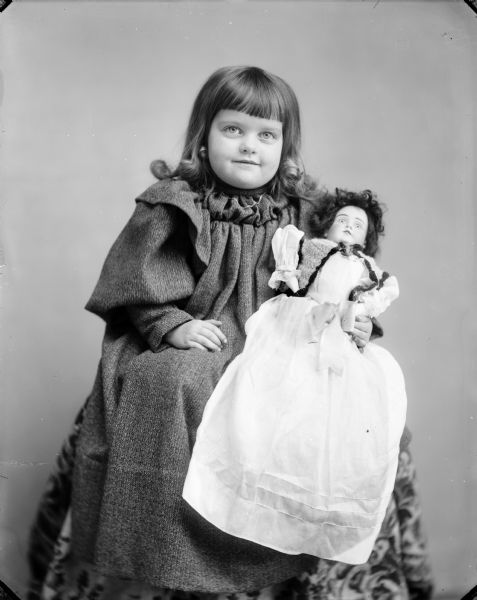 Studio portrait of a girl sitting holding a doll in her lap.